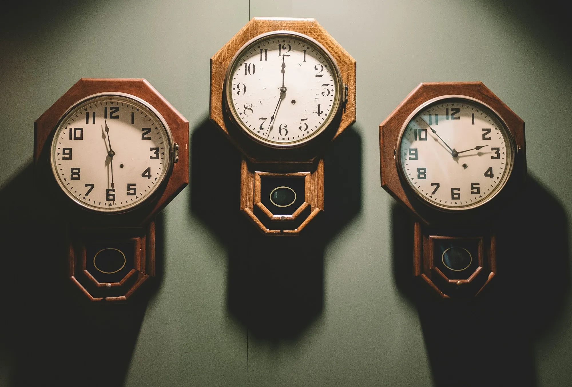 Three analog wall clocks hanging in a row on a plain wall